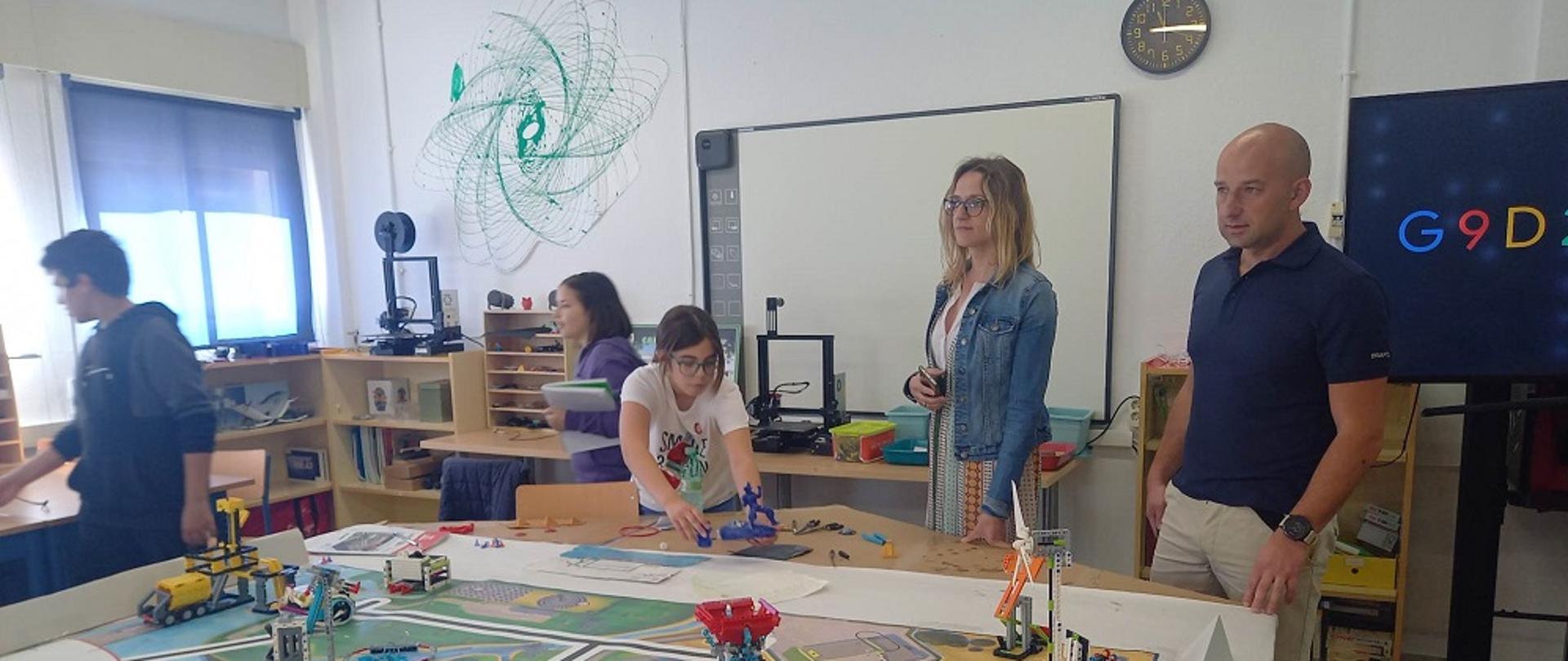 sala robotyki dwoje dorosłych i troje dzieci wokół stołu na którym stoją roboty z klocków lego 