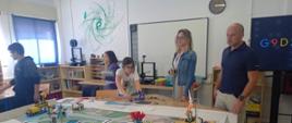 sala robotyki dwoje dorosłych i troje dzieci wokół stołu na którym stoją roboty z klocków lego 