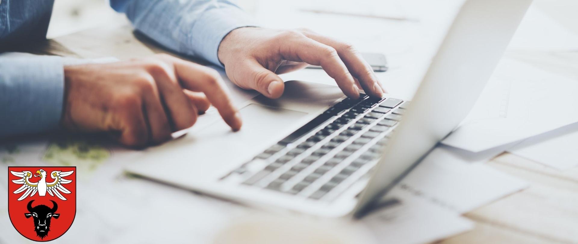 osoba obsługująca laptopa, a w lewym dolnym rogu znajduje się logo powiatu