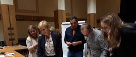 Uczestnicy spotkania podczas pracy w grupach - część warsztatowa. 5 osób pochyla się nad oznaczoną mapą 