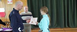 Moment przyzwania dyplomów i nagród - policjant gratuluje uczennicy