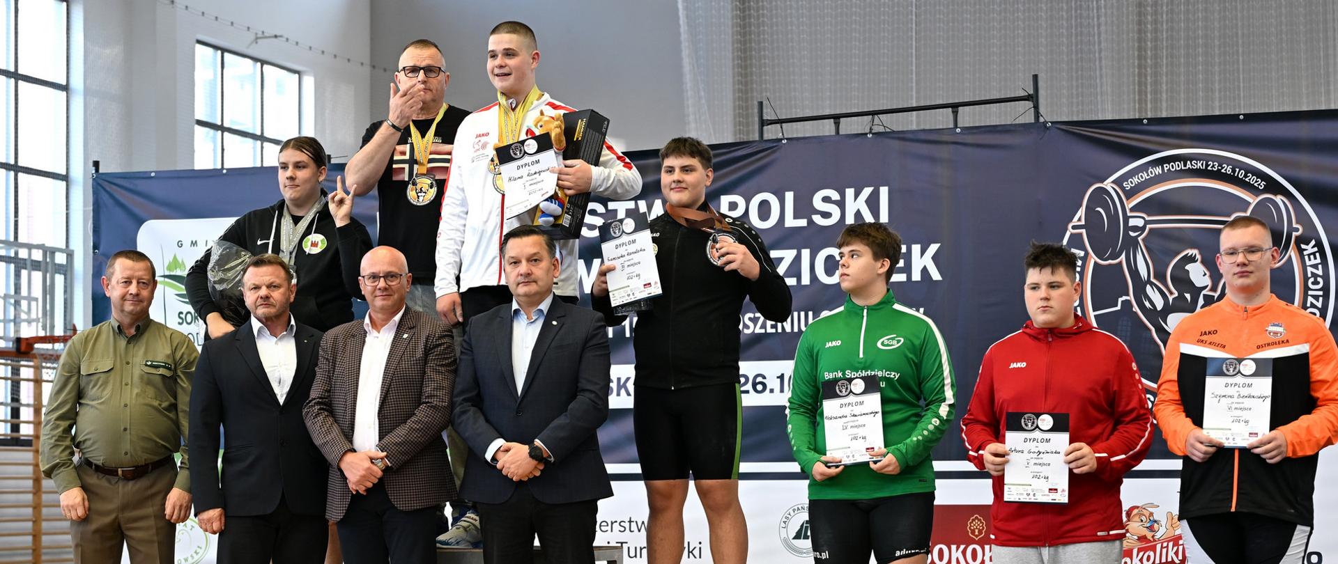 Ceremonia uhonorowania zwycięzców. Zawodnicy stoją na podium na prezentując dyplomy i medale.