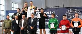 Ceremonia uhonorowania zwycięzców. Zawodnicy stoją na podium na prezentując dyplomy i medale.