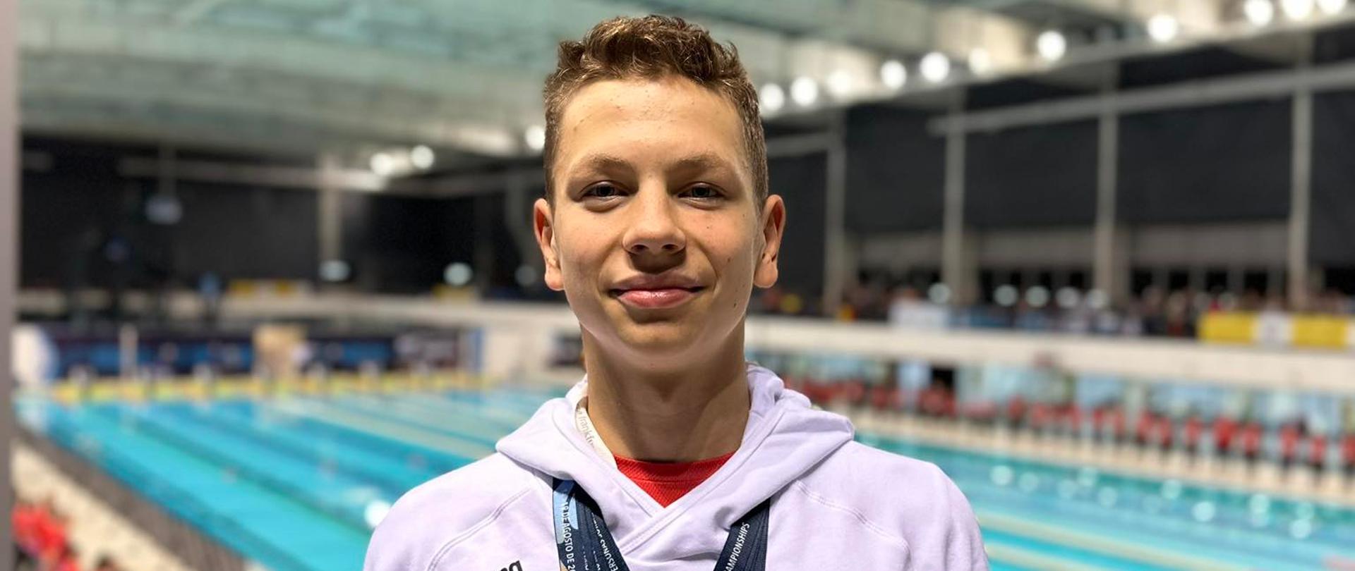 Rafał Wójcik z medalami mistrzostw świata na szyi na tle pływalni