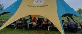Zielono żółty namiot pod którym siedzą ludzie