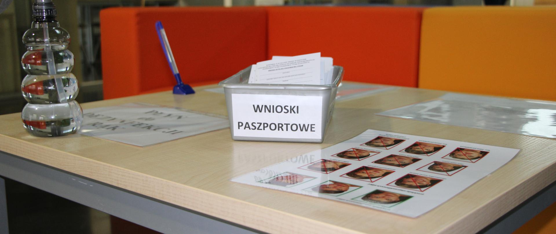 Stół, na którym leżą wnioski paszportowe, długopis, zdjęcia oraz płyn do dezynfekcji rąk