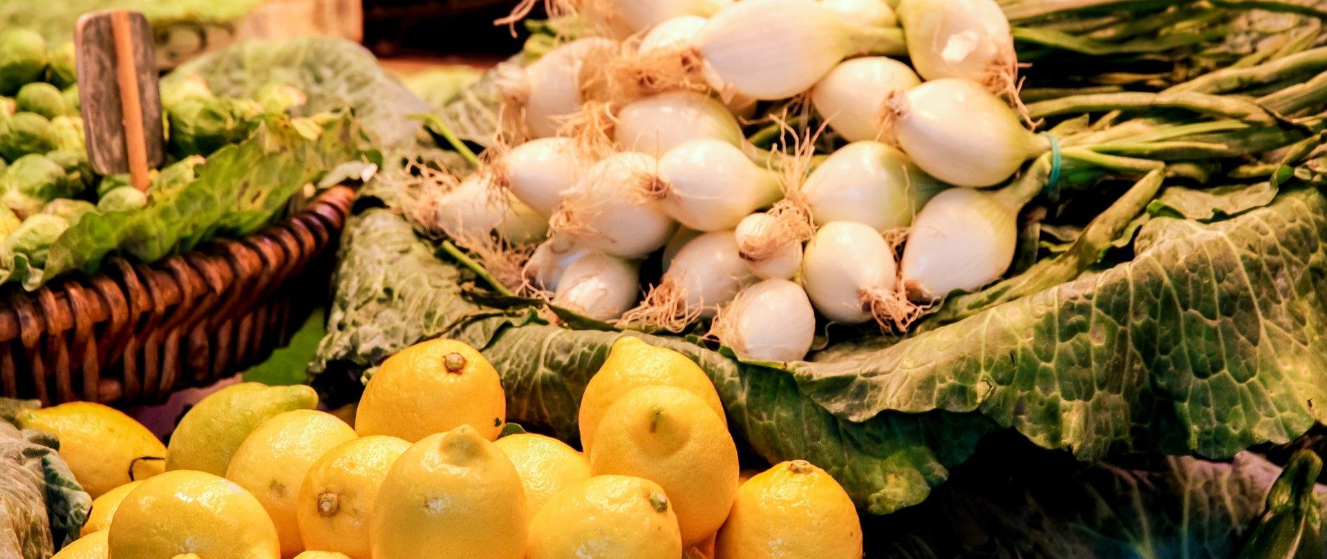 Zdjęcie przedstawia warzywa i owoce na targowisku. Warzywa i owoce ujęte na zdjęciu to cebula i cytryny.