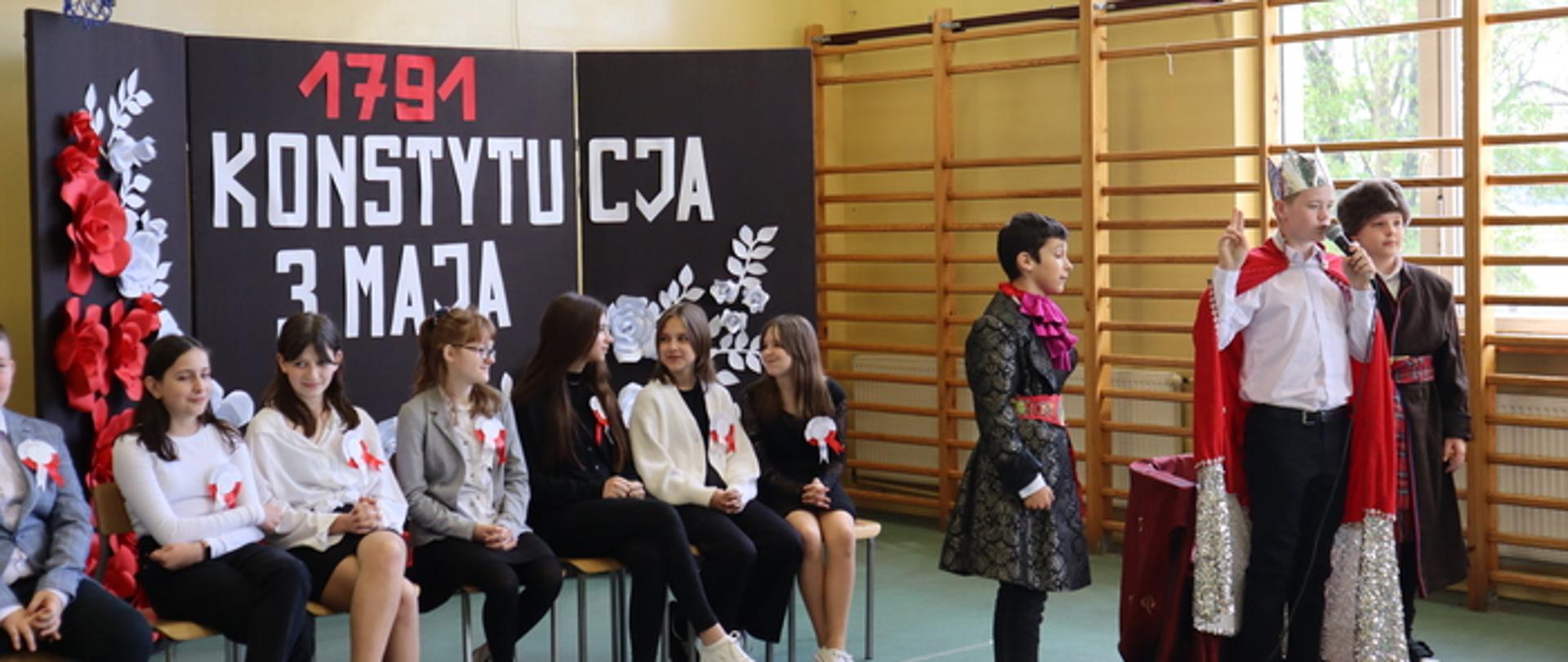Inscenizacja artystyczna z okazji święta Konstytucji 3 Maja. Uczniowie w kostiumach króla, szlachty i mieszczaństwa.