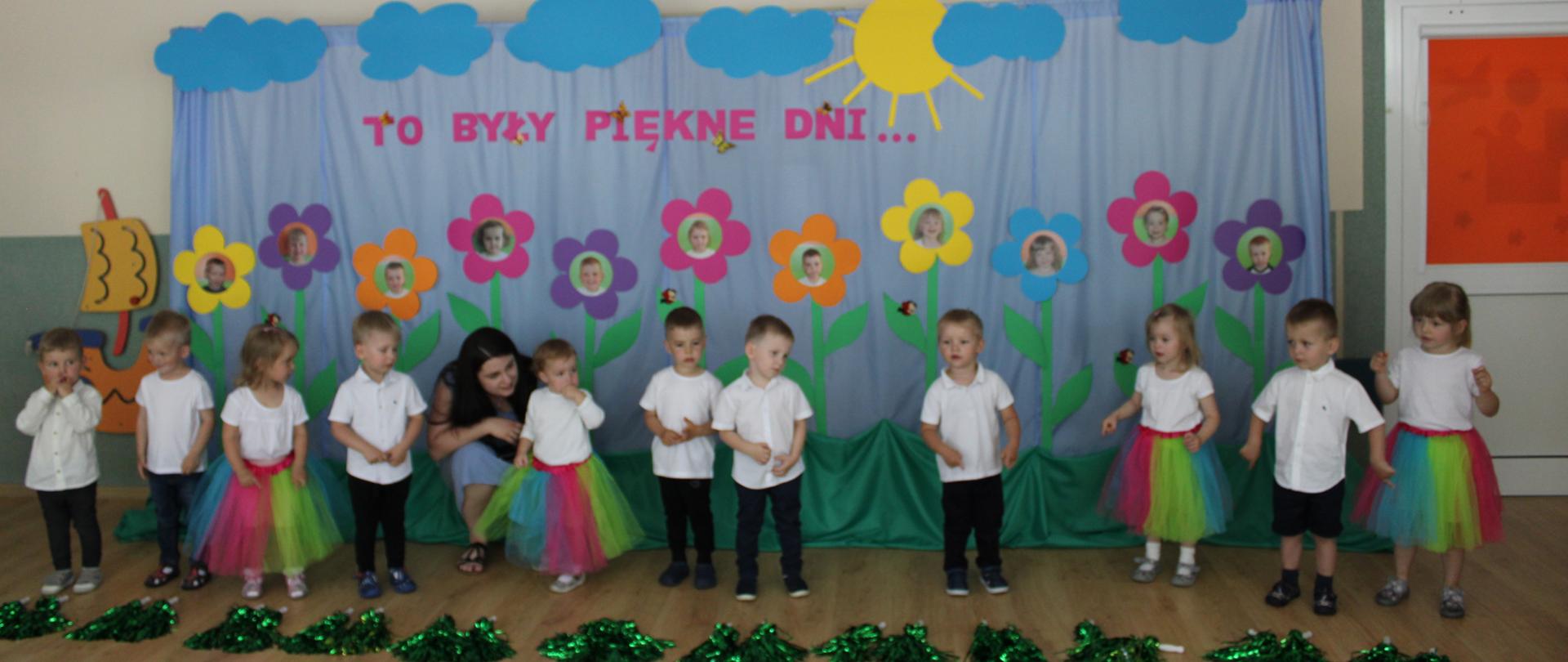 Na zdjeciu widać grupę dzieci odświętnie ubranych, w tlr widać piękną dekorację, składającą się z kwiatków ze zdjęciami dzieci.