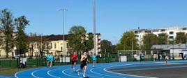Sześcioro uczniów ubranych w stroje sportowe biegnie po stadionie lekkoatletycznym.