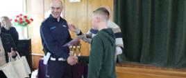 Moment przyzwania dyplomów i nagród - policjant gratuluje uczniowi