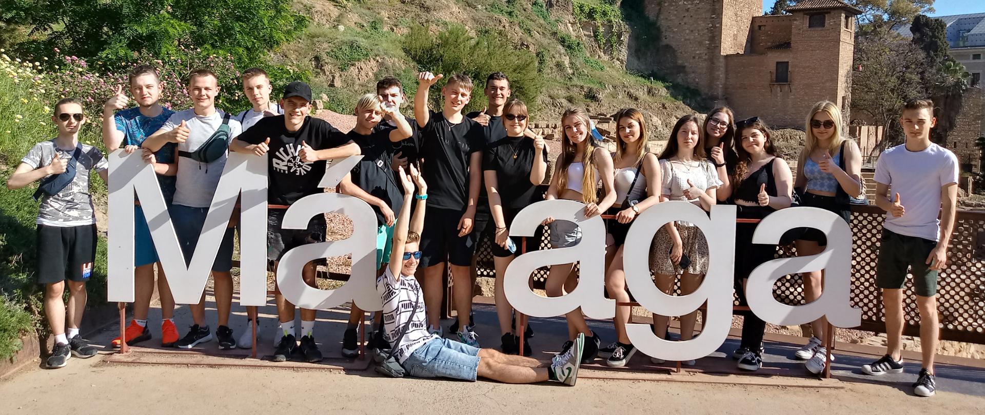 Grupa uczniów Zespołu Szkół w Chocianowie pozuje do zdjęcia z napisem Malaga w Hiszpanii podczas wyjazdu na staż