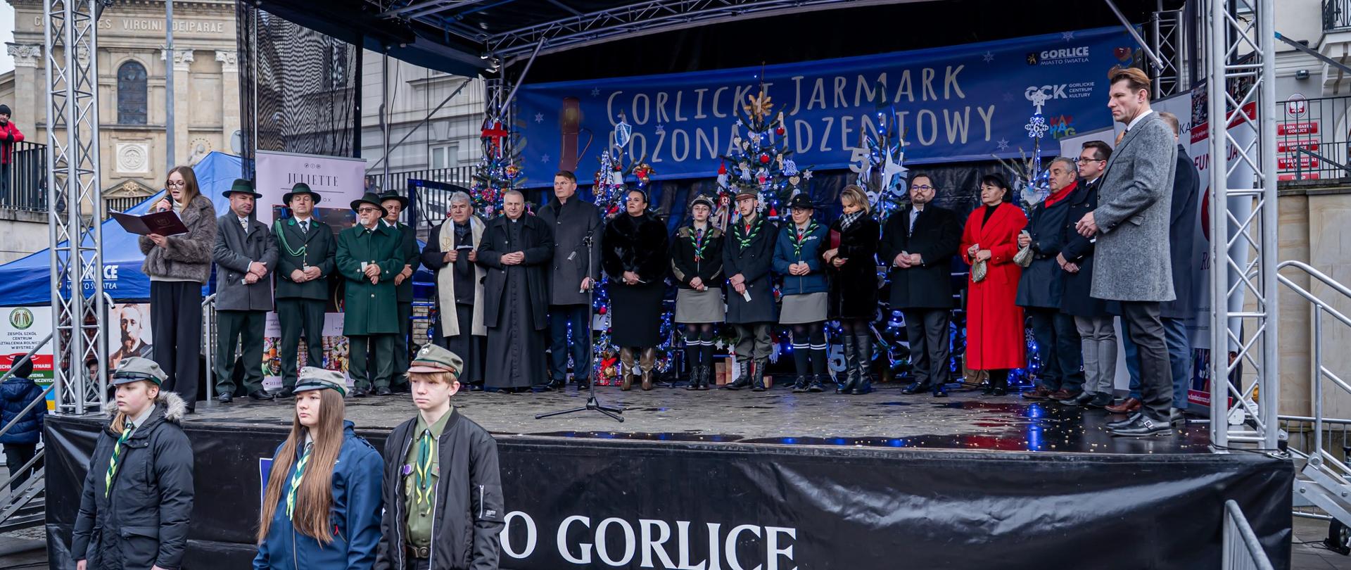 Na scenie organizatorzy i fundatorzy XIV Wigilii, przed sceną stoi trójka harcerzy
