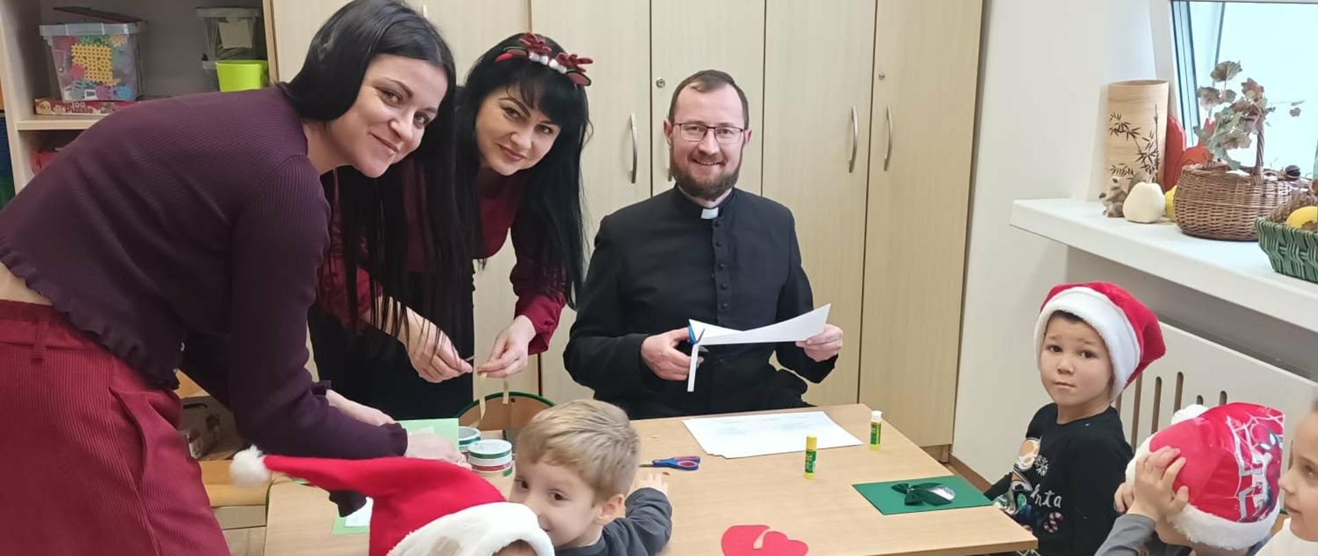 Nauczyciele i dzieci siedzą przy stolikach wkonując kartki