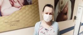 Mama z noworodkiem leżącym w łóżeczku na szpitalnym korytarzu oddziału ginekologiczno-położniczego w szpitalu powiatowym. Mama trzyma w ręku upominki dla dziecka od Powiatu Pruszkowskiego. 