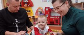 Rodzice z dzieckiem siedzą przy stole, tworzą świąteczne ozdoby