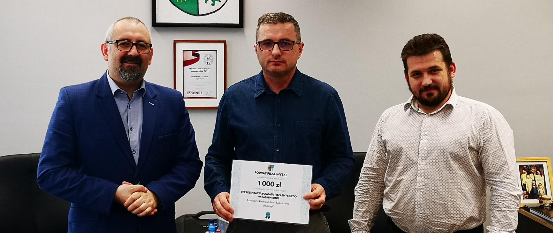 Jednorożecki Klub Badmintona „BadKurp” otrzymał dofinansowanie na reprezentowanie Powiatu Przasnyskiego w badmintonie. Zdjęcie wykonane w gabinecie Starosty w Przasnyszu. Po lewej Starosta Przasnyski Krzysztof Bieńkowski, w środku przedstawiciel "Badkurp", po prawej Etatowy Członek Zarządu Powiatu Paweł Mostowy.