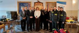 Grupowe zdjęcie uczestników uroczystego przekazania sprzętu dla jednostek OSP z Gminy Raba Wyżna - przedstawiciele władz gminy, administracji rządowej oraz strażacy na tle przekazanego sprzętu. 