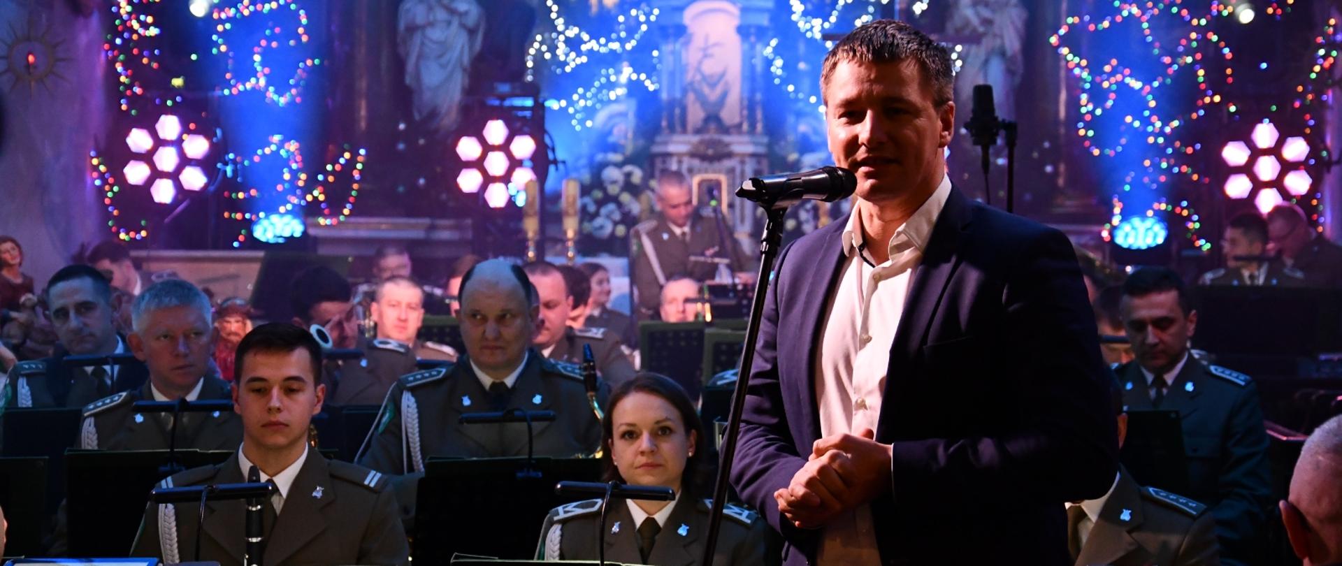 orkiestra w mundurach siedząca w kościele, w tle ołtarz, na pierwszym planie zastępca burmistrza Miasta i Gminy Margonin