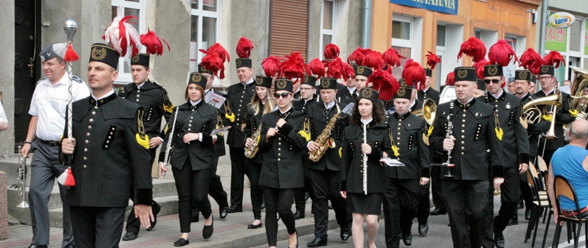 Pokaz musztry paradnej w wykonaniu Orkiestry Kopalni Węgla Brunatnego z Konina. Orkiestra w pełnym składzie przechodzi ulicami miasta dookoła rynku w Margoninie. Ubrani są w czarne mundury z ozdobnymi czerwonymi pióropuszami na czubkach czapek.