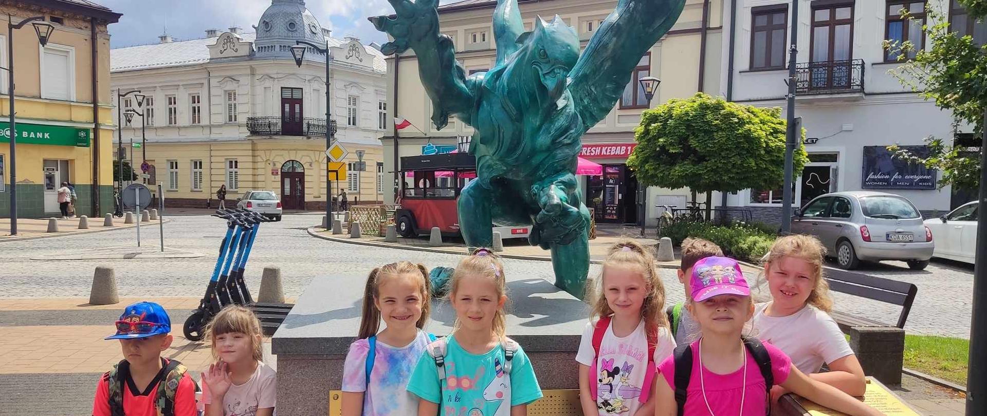 Uczniowie stoją przy pomniku Gryfa na mielelckiej Starówce.