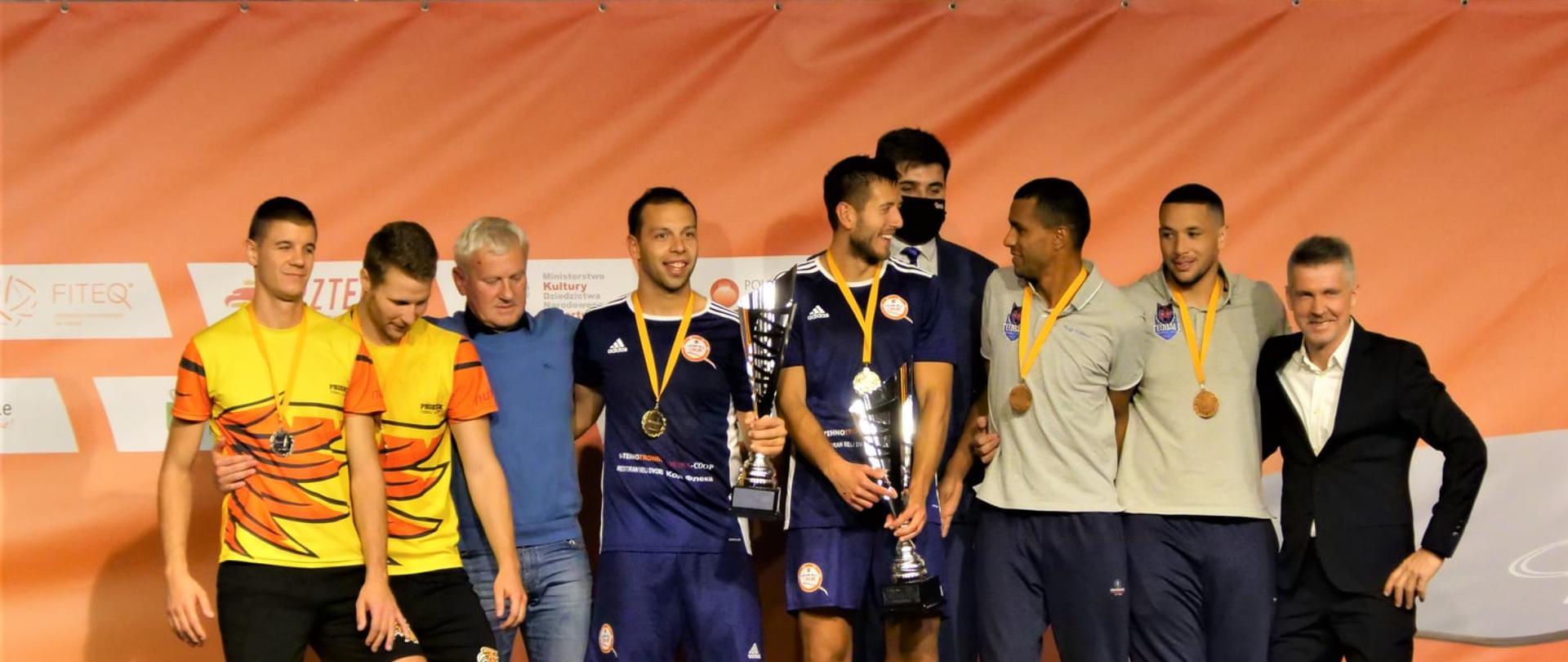 Dziewięć osób stoi na podium wewnątrz budynku (hali sportowej). Dekoracja zwycięzców podczas EUROPEAN TEQBALL TOUR - JÓZEF BEM CHELM Trophy.