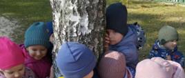 Dzieci i nauczycielki przytulają się do drzewa