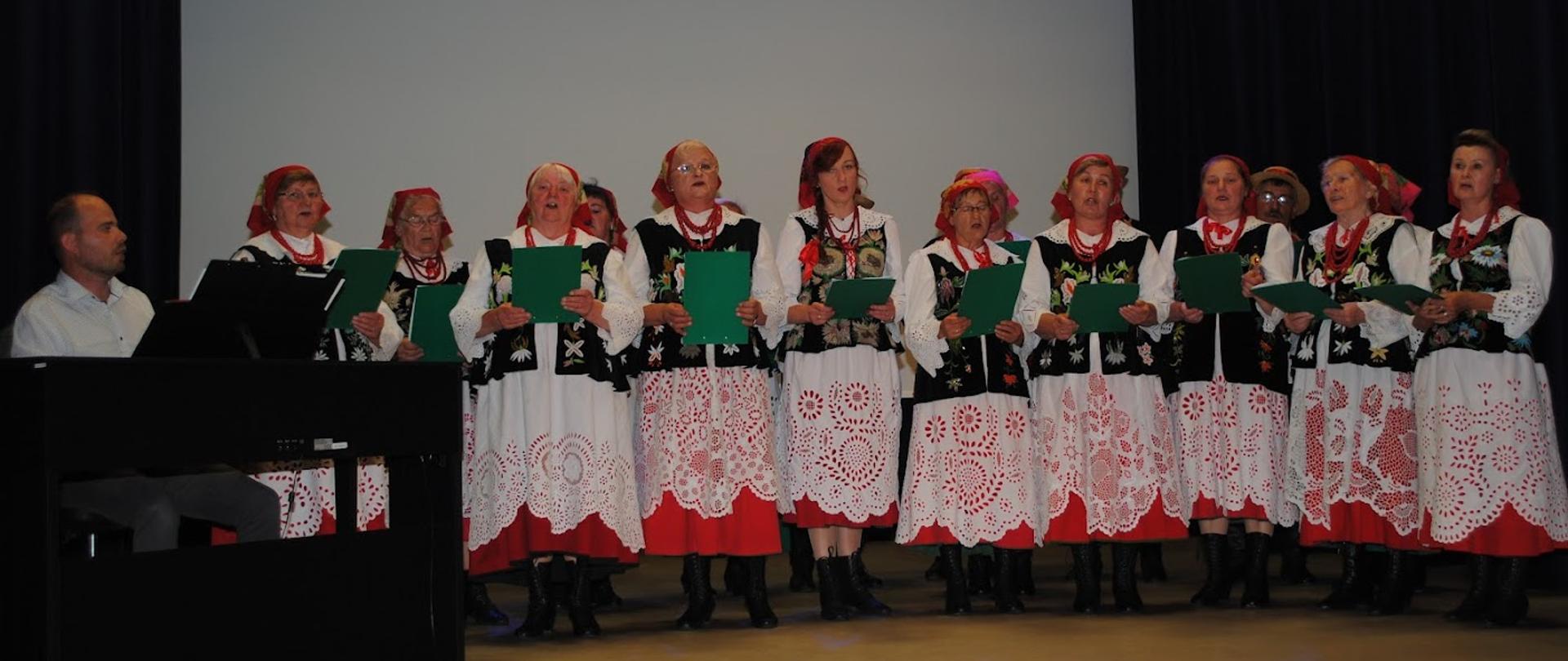 zespół kobiet ubranych w kolorowe ludowe stroje, śpiewających na scenie