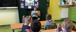 Dziewczynka na krześle czyta książkę dla pozostałych uczniów w klasie
