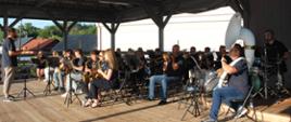 mężczyźni i kobiety siedzą na krzesełkach i grają na instrumentach muzycznych 