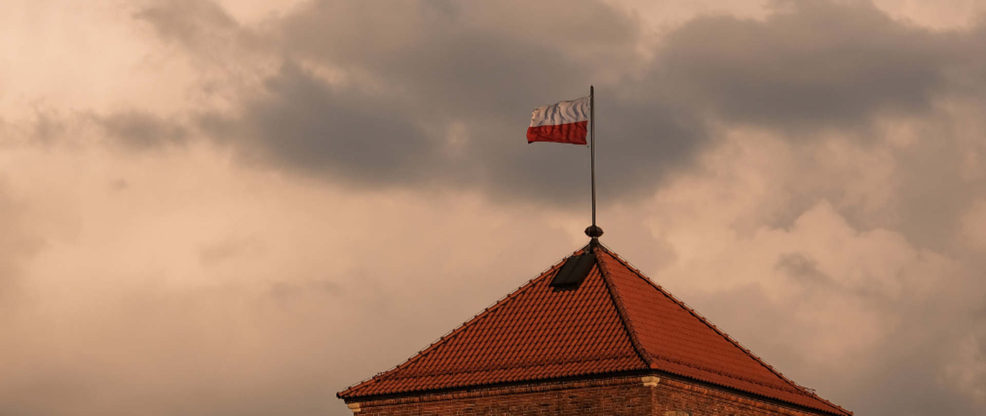 Zdjęcie dachu czerwonego a nim powiewająca flaga Polski
