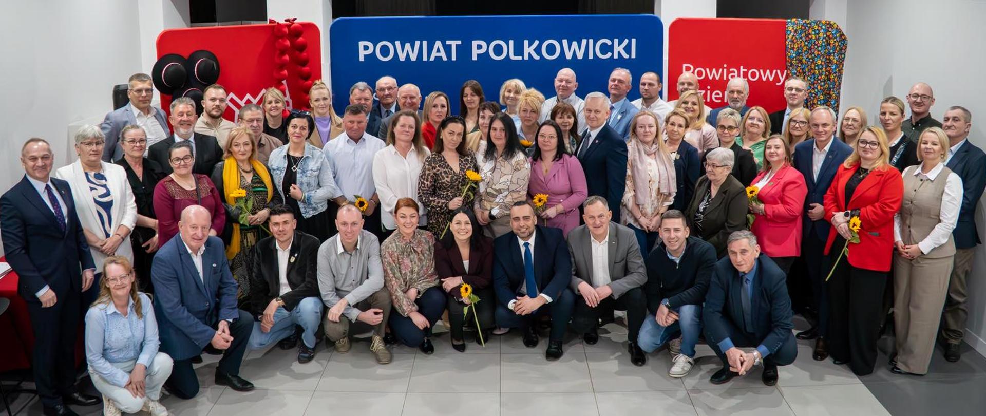 Osoby stoją i uśmiechają się do zdjęcia grupowego.