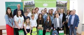 Zdjęcie grupowe laureatów konkursu z organizatorami oraz rodzicami i opiekunami. Dzieci i młodzież wraz z pozostałymi osobami obecnymi podczas uroczystości pozują do fotografii ma tle ścianki, na której widoczny jest logotyp oraz napis powiat sokołowski. Dzieci w dłoniach trzymają zdobyte w konkursie nagrody.