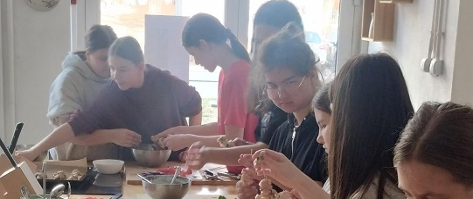 Dziewczyny stoją przy wyspie kuchennej. przed nimi stoją miski i deski do krojenia