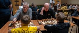 Uczestnicy podczas turnieju - siedzą przy stołach rozgrywają partię szachów