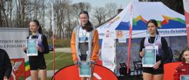 Monika obok dwóch zawodniczek, stoi na podium, trzyma dyplom
