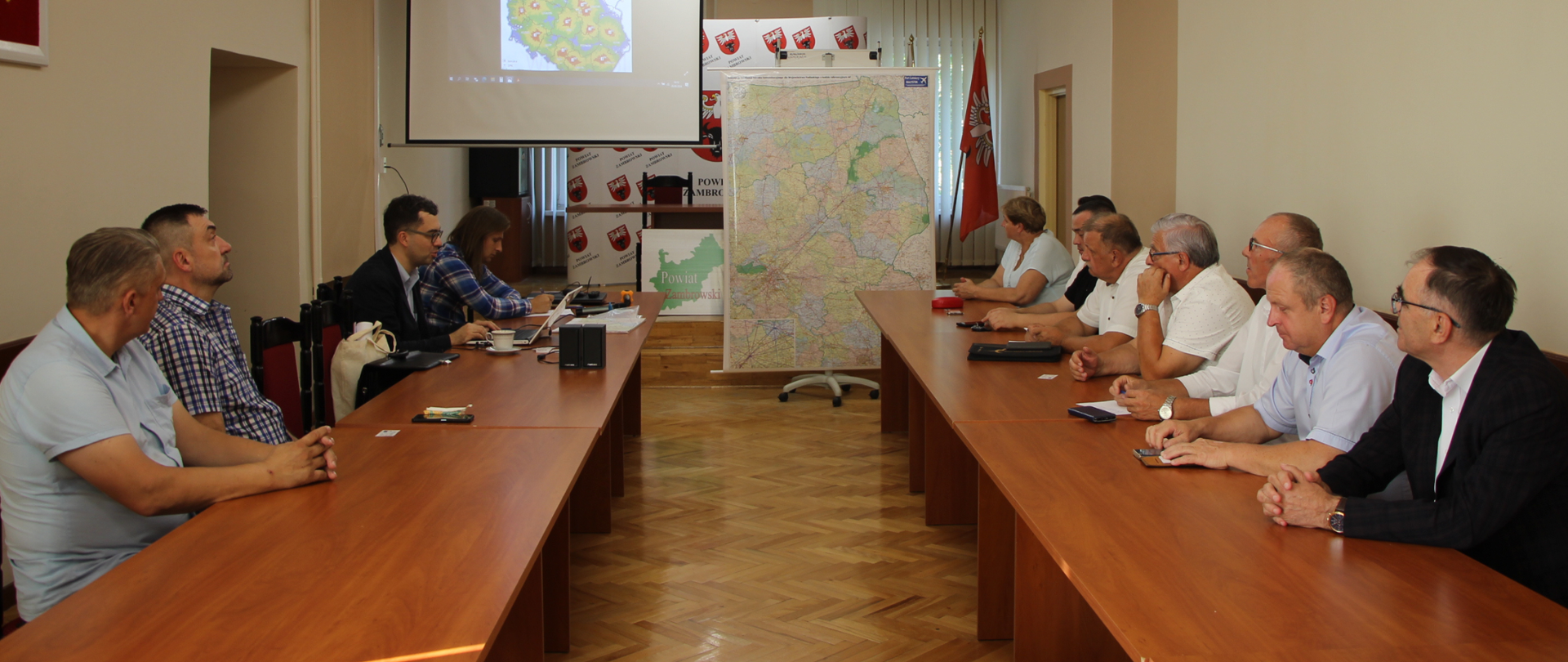 na zdjęciu znajdują się radni powiatu zambrowskiego oraz przedstawiciel Stowarzyszenia Port Lotniczy Białystok Pan Karol Halicki, którzy siedzą w sali konferencyjnej Starostwa Powiatowego w Zambrowie podczas spotkania dotyczącego budowy lądowiska i lotniska