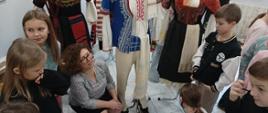 Kobieta kuca przy manekinach ubranych w stroje ludowe
