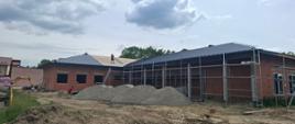 budynek z czerwonej cegły, z otworami na okna, i częściowym grafitowym dachem, przed budynkiem metalowe rusztowanie i hałdy pisaku 