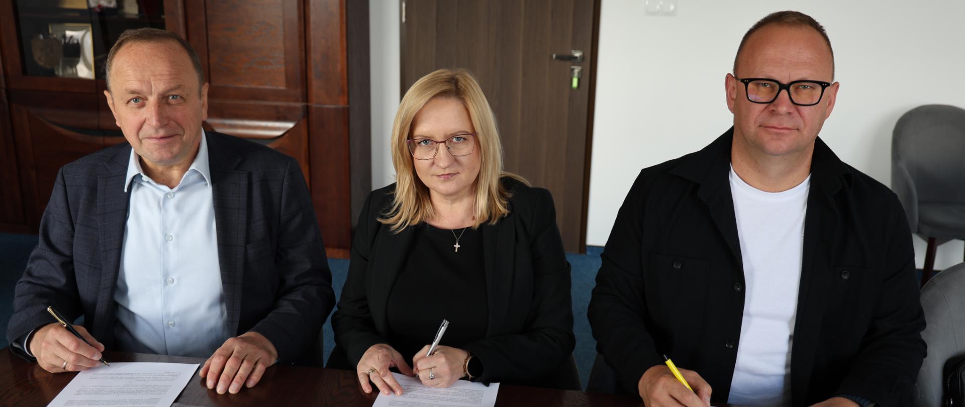 Trzy osoby podpisują umowę na realizację inwestycji.