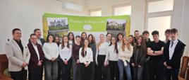Uczniowie wraz ze starostą i pozostałymi uczestnikami pozują do grupowego zdjęcia na tle ścianki w sali konferencyjnej Starostwa Powiatowego w Sokołowie Podlaskim