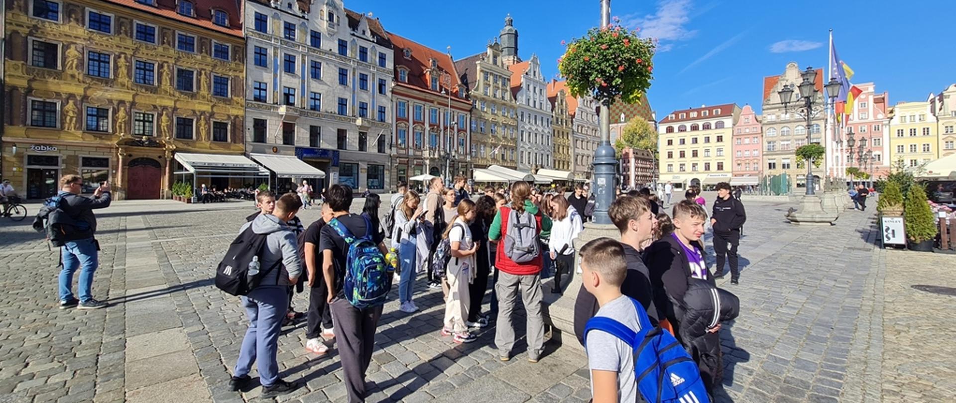 Grupa dzieci na rynku wrocławskim. Wokół rynku widać piękne zabytkowe, kolorowe kamienice.