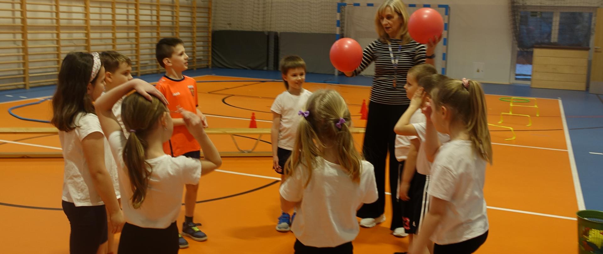 Uczniowie na sali gimnastycznej wykonują ćwiczenia z piłką