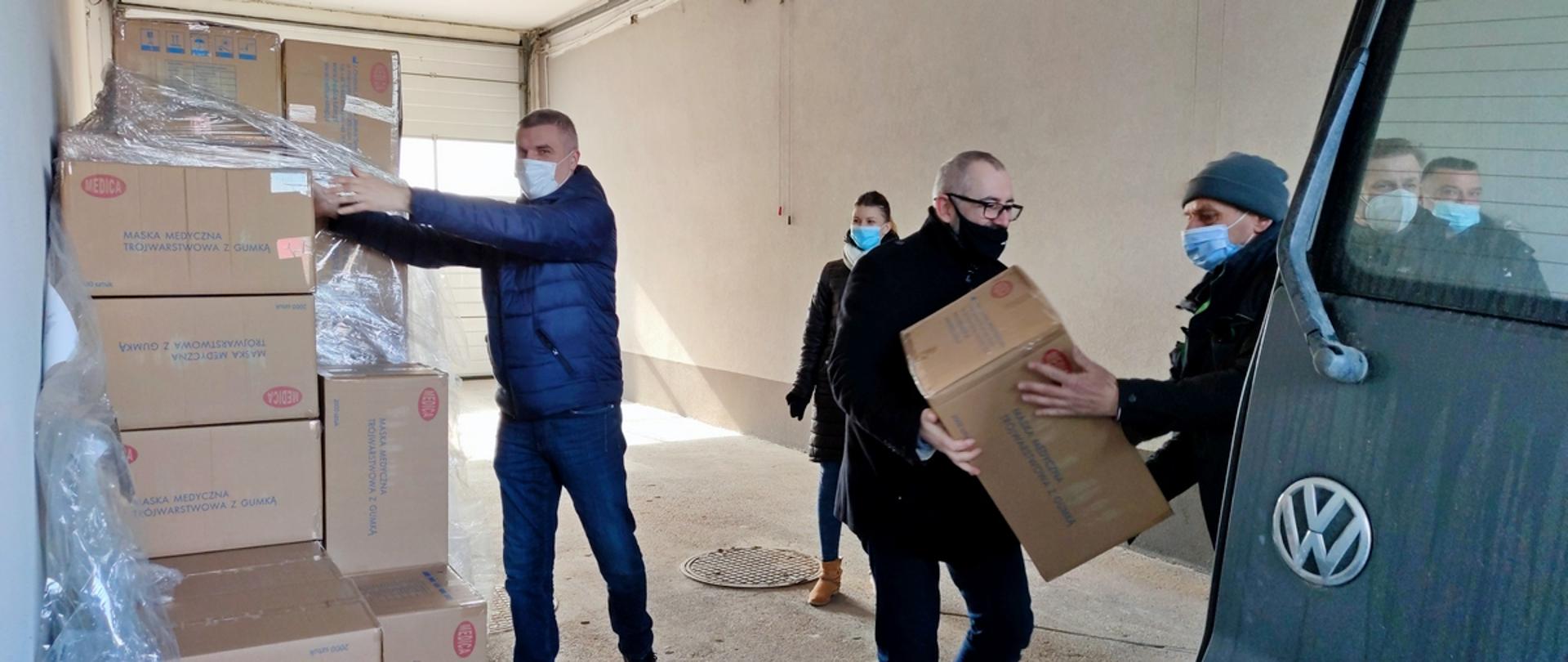 Starosta Przasnyski Krzysztof Bieńkowski wraz z pracownikami Referatu Zarządzania Kryzysowego Starostwa Powiatowego w Przasnyszu rozpakowuje transport maseczek z Agencji Rezerw Materiałowych.