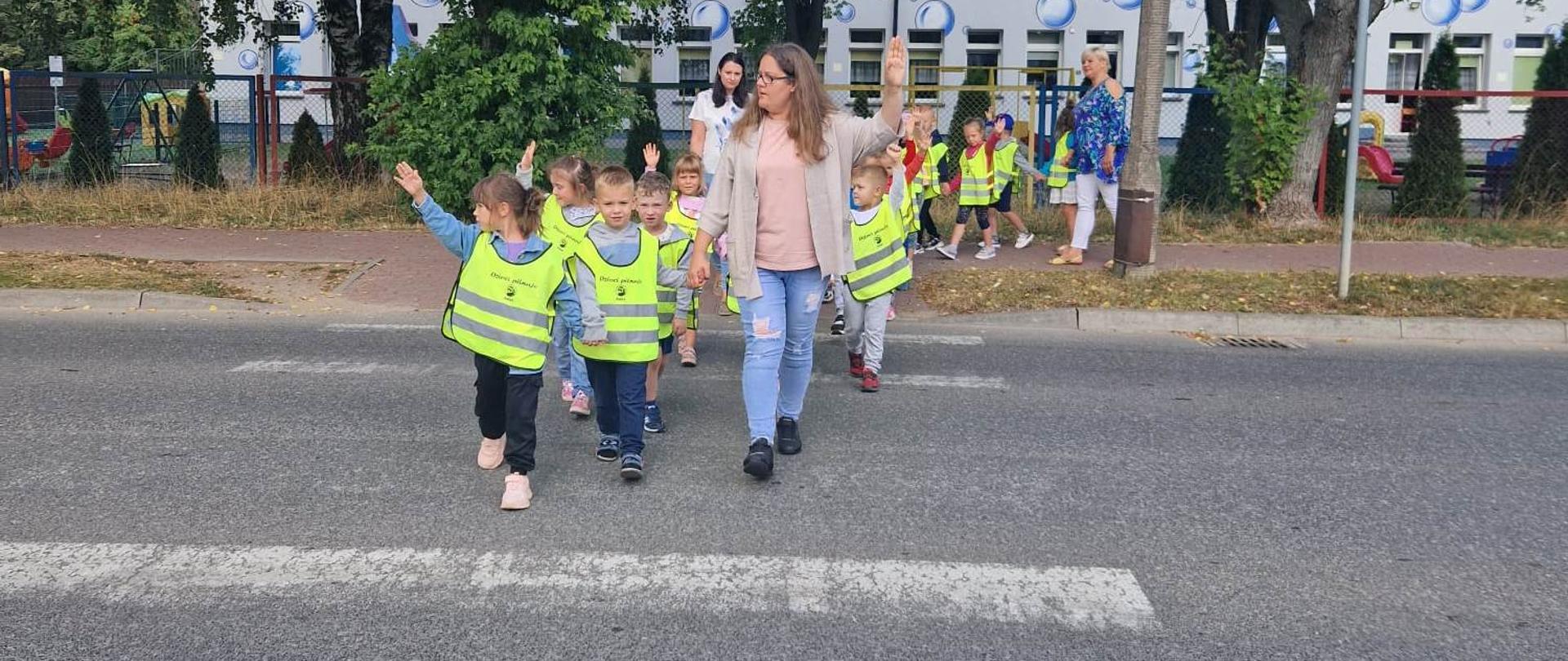 1 osoba dorosła i grupa dzieci w odblaskowych kamizelkach na przejściu dla pieszych