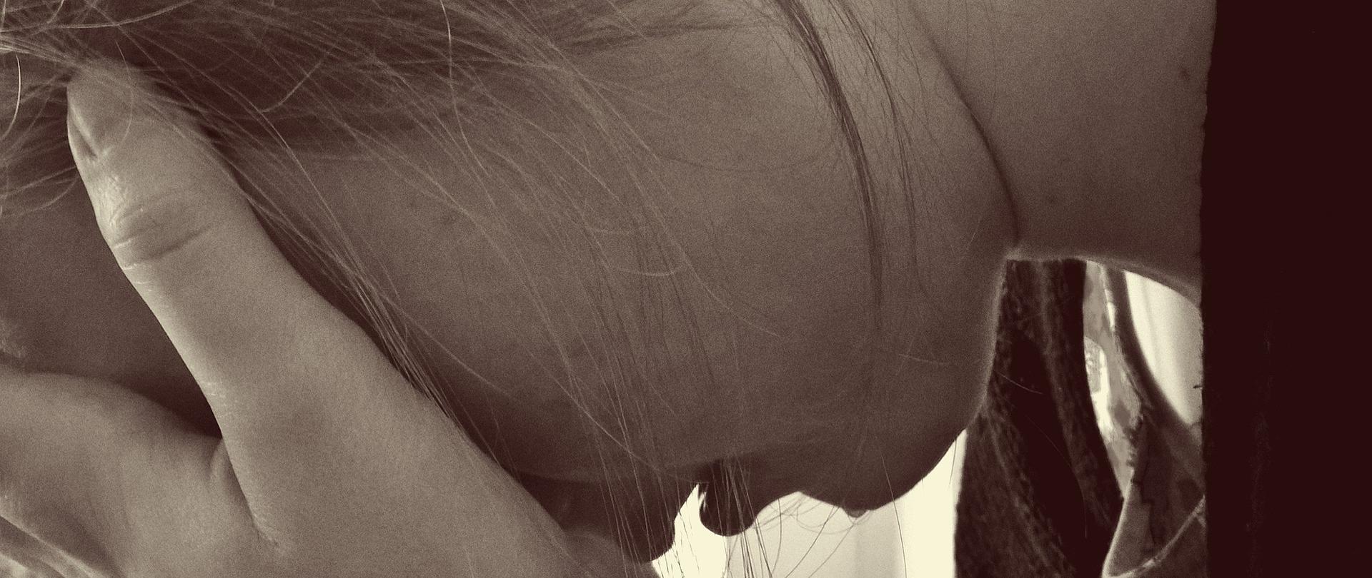 Przemoc w rodzinie (zdjęcie ilustracyjne). Na czarno-białej fotografii widoczna młoda dziewczyna z twarzą ukrytą w dłoniach.