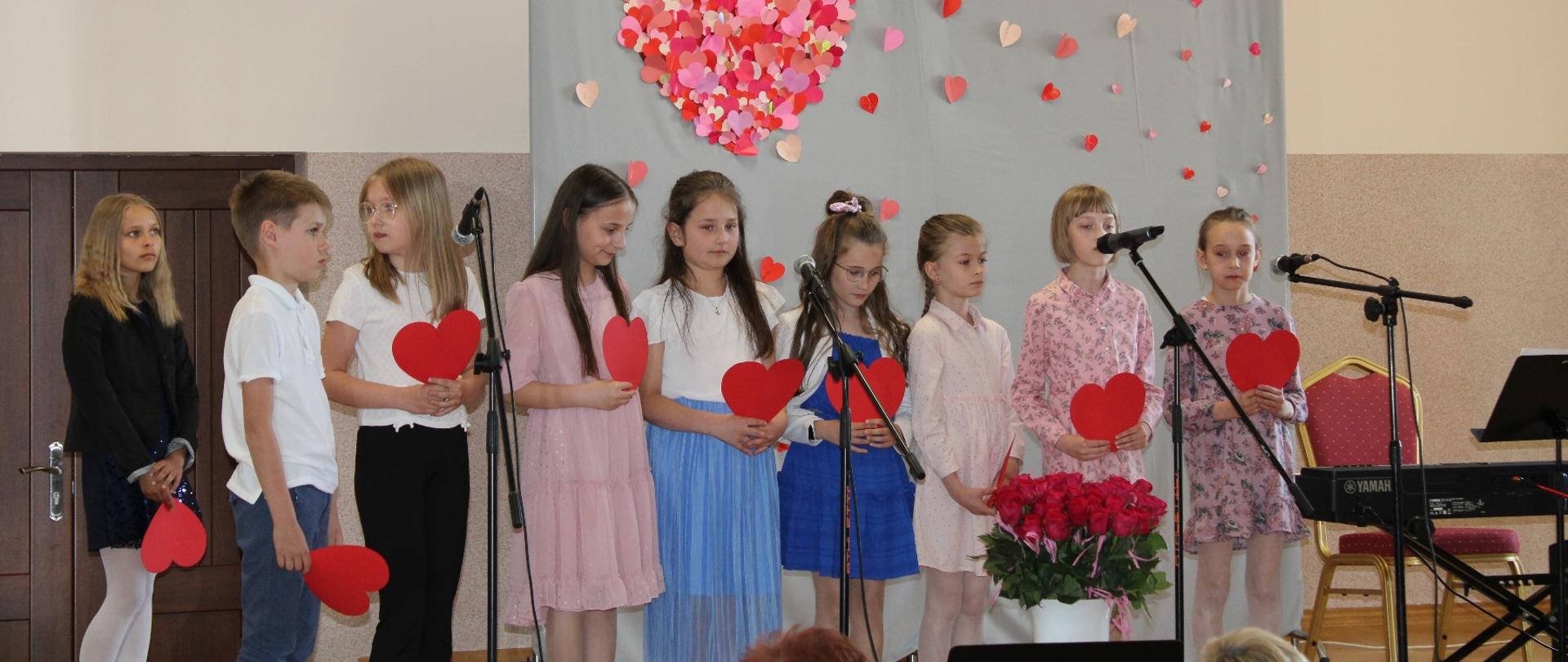 Dziewczynki ustawione w rzędzie, w rękach trzymają przed sobą czerwone serca