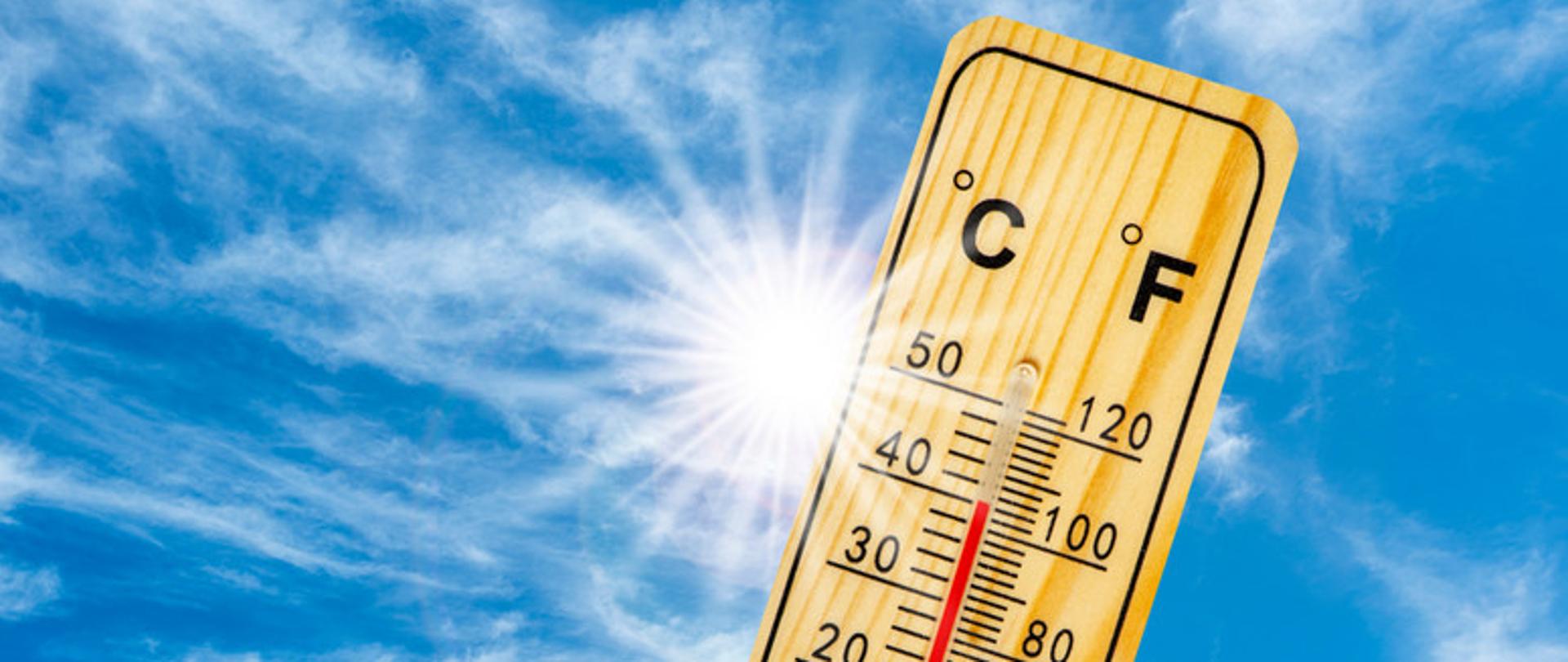 Zdjęcie przedstawia termometr wskazujący wysoką temperaturę, na tle niebieskiego słonecznego nieba