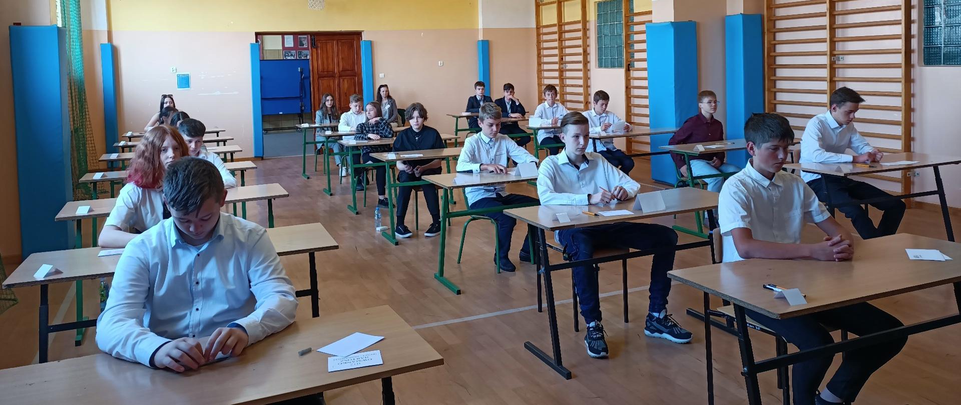 Dzieci siedzące przy porozsuwanych ławkach