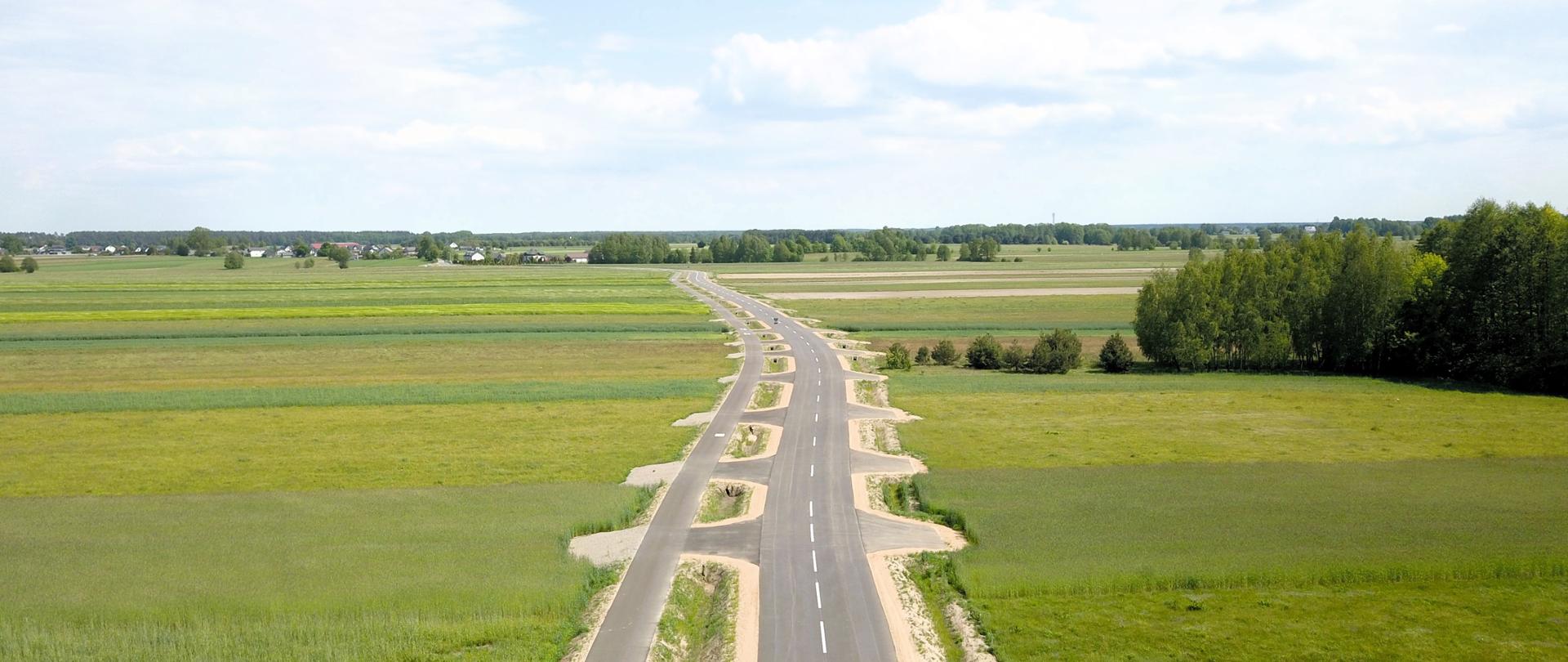 Widok z lotu ptaka na drogę pośród pól ze zjazdami, rowem przydrożnym i ścieżką pieszo-rowerową